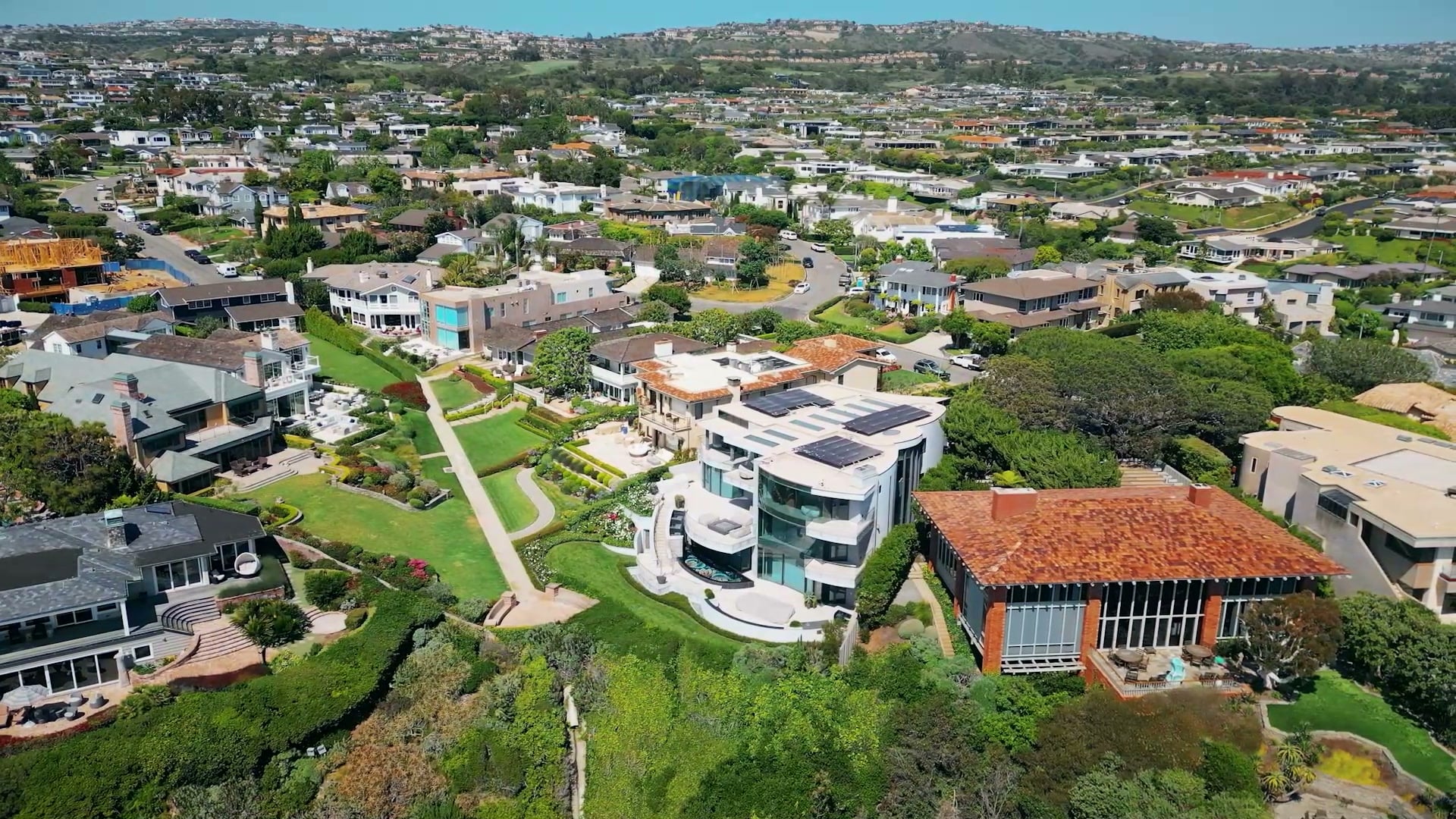 Aerial view of contemporary and tile-roofed houses with terraced gardens on a green bluff