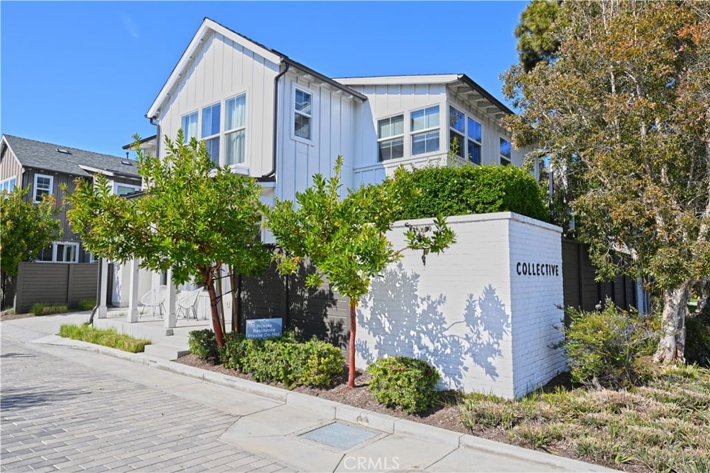 A white two-story house with board-and-batten siding on a street corner, behind young trees